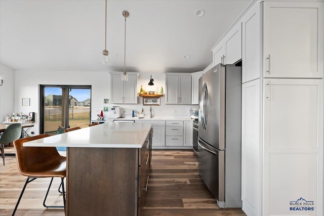 kitchen with a kitchen breakfast bar, dark hardwood / wood-style flooring, pendant lighting, a center island, and stainless steel refrigerator