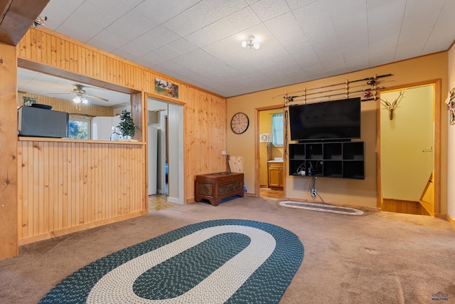 interior space with ceiling fan, wood walls, and light carpet