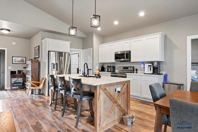 kitchen featuring appliances with stainless steel finishes, vaulted ceiling, a kitchen island with sink, pendant lighting, and white cabinetry