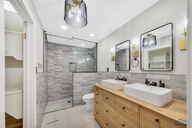 bathroom with tile patterned floors, a tile shower, vanity, tile walls, and toilet