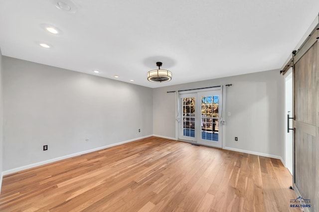 empty room with a barn door, light hardwood / wood-style flooring, a healthy amount of sunlight, and french doors