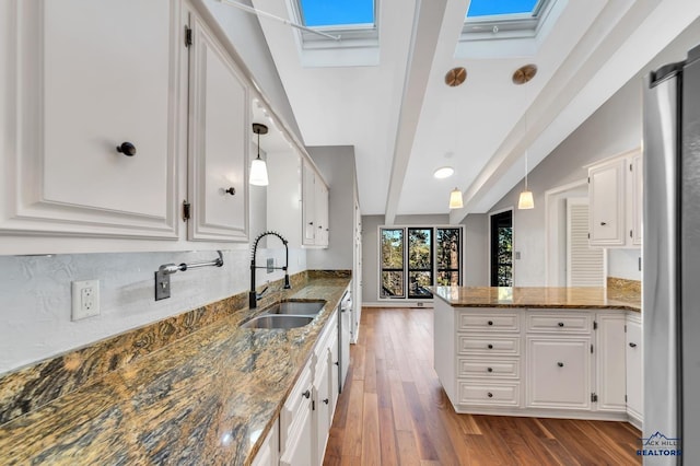 kitchen with kitchen peninsula, sink, decorative light fixtures, dark stone countertops, and white cabinetry