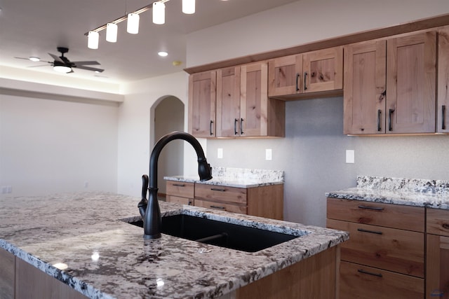 kitchen featuring ceiling fan, light stone counters, hanging light fixtures, and sink