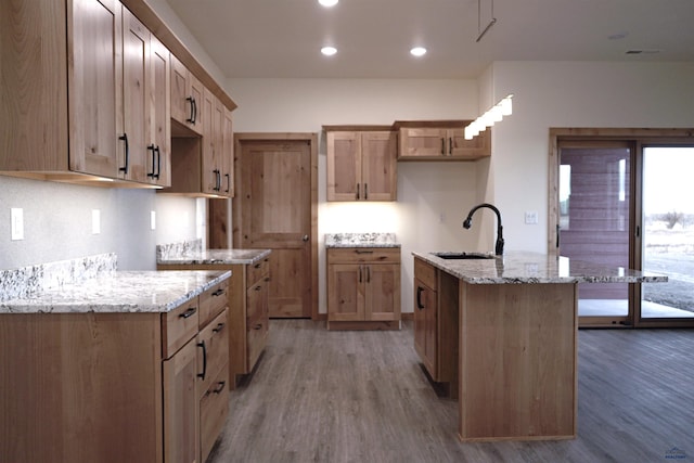 kitchen featuring dark hardwood / wood-style flooring, light stone countertops, sink, and an island with sink