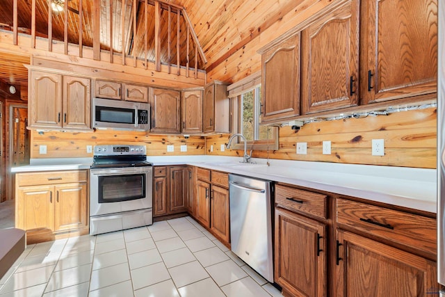 kitchen with light tile patterned floors, sink, stainless steel appliances, and wood walls