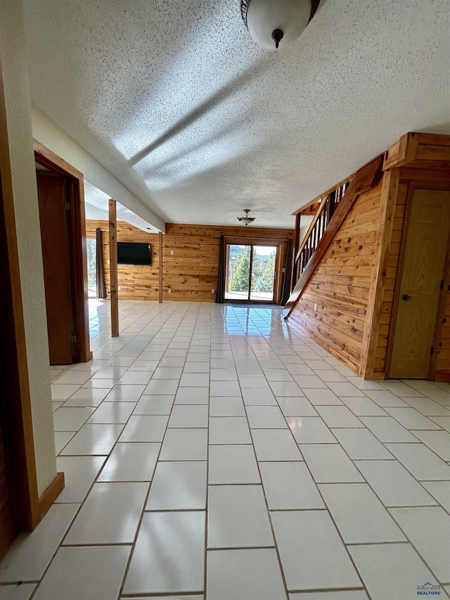 interior space with light tile patterned flooring, a textured ceiling, and wooden walls