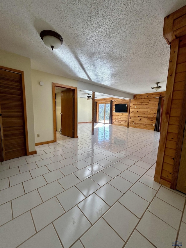 empty room with light tile patterned flooring, a textured ceiling, ceiling fan, and wood walls