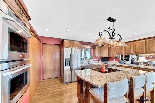 kitchen featuring light stone counters, appliances with stainless steel finishes, pendant lighting, a kitchen island, and light wood-type flooring