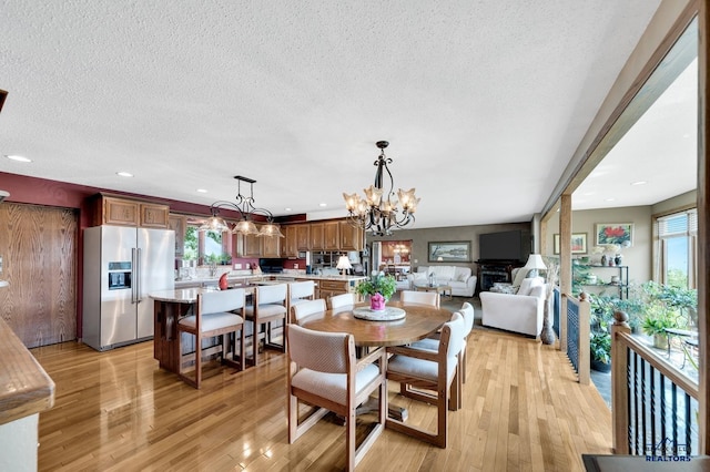 dining room featuring light wood-type flooring, a textured ceiling, and a notable chandelier