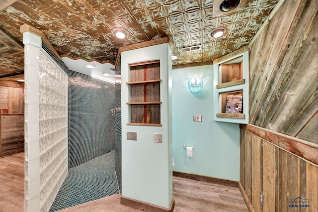 bathroom with a tile shower, wood walls, and hardwood / wood-style flooring