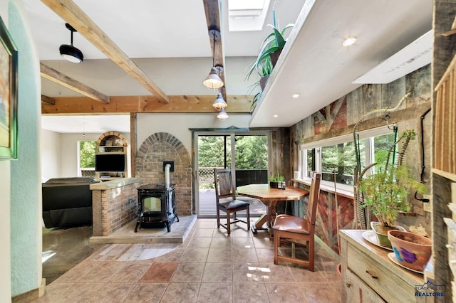 tiled dining area featuring a wood stove, beamed ceiling, and a skylight