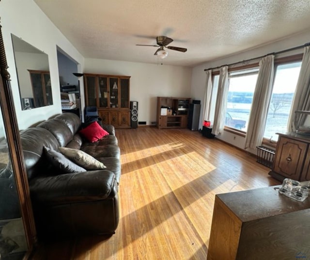 living room with ceiling fan, radiator heating unit, light wood-type flooring, and a textured ceiling