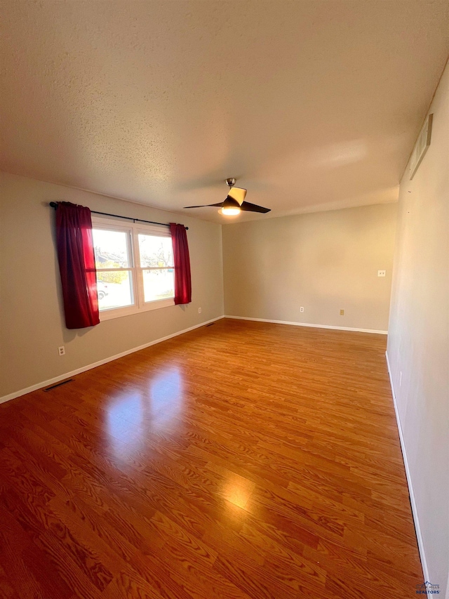 spare room featuring visible vents, baseboards, a ceiling fan, wood finished floors, and a textured ceiling