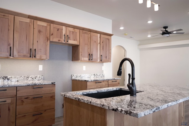 kitchen with light stone countertops, ceiling fan, sink, hardwood / wood-style flooring, and an island with sink