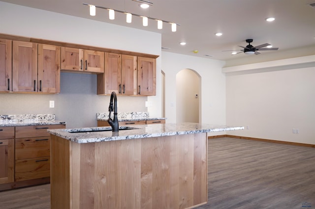 kitchen featuring a center island with sink, sink, dark hardwood / wood-style floors, ceiling fan, and light stone countertops