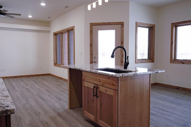 kitchen with ceiling fan, light stone countertops, sink, an island with sink, and light wood-type flooring