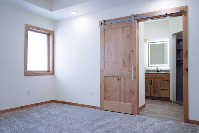 unfurnished bedroom featuring a barn door, sink, light carpet, and ensuite bath