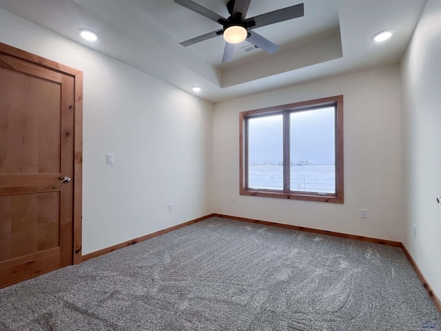 carpeted empty room with ceiling fan and a tray ceiling