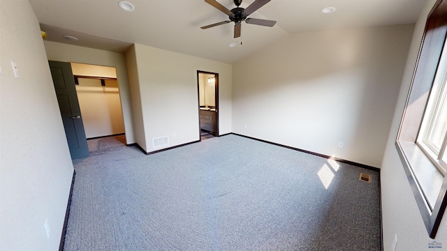 unfurnished bedroom featuring ceiling fan, dark colored carpet, connected bathroom, vaulted ceiling, and a closet