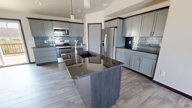 kitchen featuring sink, gray cabinetry, stainless steel appliances, a center island with sink, and decorative light fixtures