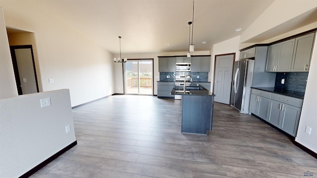 kitchen featuring gray cabinetry, tasteful backsplash, an island with sink, pendant lighting, and stainless steel appliances