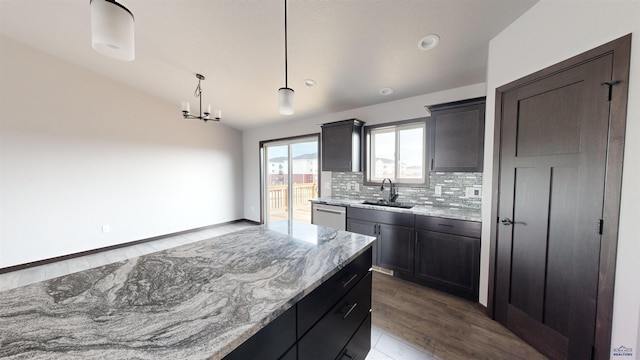 kitchen featuring pendant lighting, dishwasher, sink, vaulted ceiling, and light stone counters