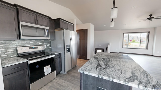 kitchen with light stone countertops, ceiling fan, stainless steel appliances, pendant lighting, and vaulted ceiling