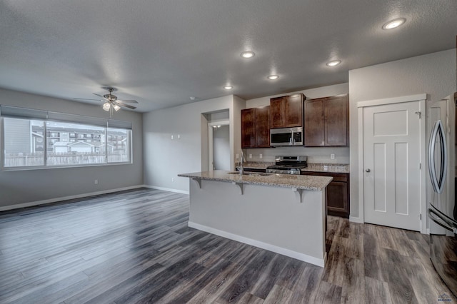 kitchen featuring a kitchen island with sink, sink, a textured ceiling, appliances with stainless steel finishes, and a breakfast bar area