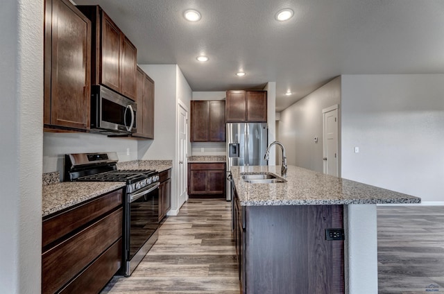 kitchen with a kitchen island with sink, sink, light wood-type flooring, dark brown cabinetry, and stainless steel appliances