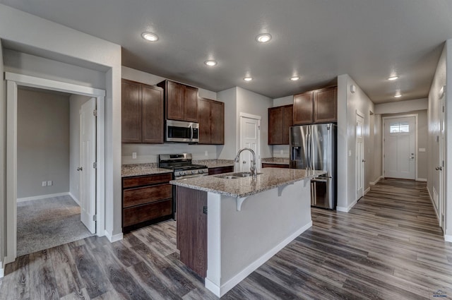 kitchen with a breakfast bar, a center island with sink, sink, dark hardwood / wood-style flooring, and stainless steel appliances