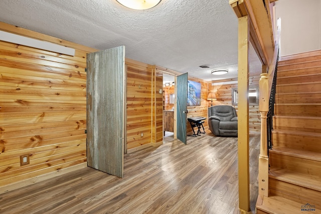 interior space with wooden walls, a textured ceiling, and hardwood / wood-style flooring