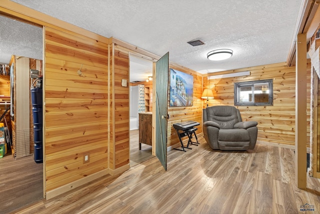 sitting room featuring wood-type flooring, a textured ceiling, and wooden walls