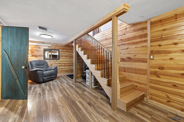 staircase featuring wood-type flooring, a textured ceiling, and wood walls