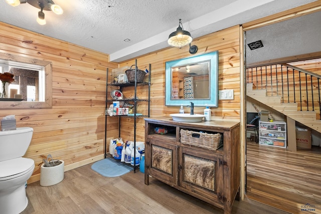 bathroom featuring hardwood / wood-style floors, vanity, wooden walls, toilet, and a textured ceiling