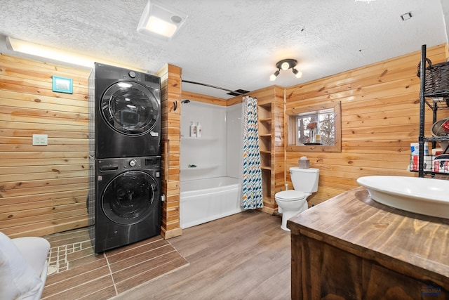 full bathroom with vanity, hardwood / wood-style flooring, stacked washer / dryer, toilet, and wood walls