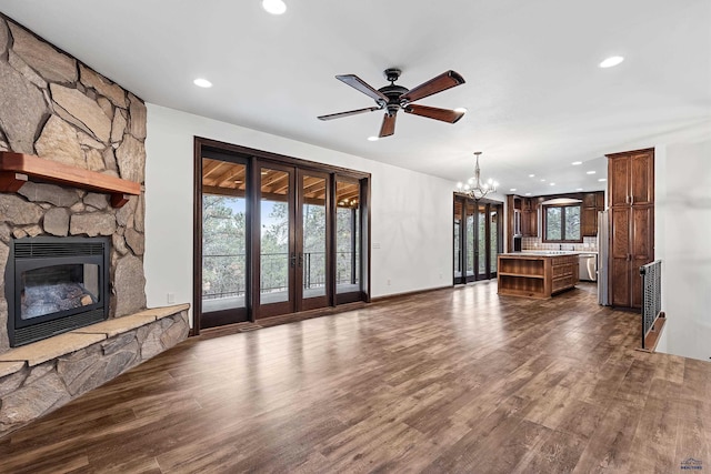 unfurnished living room with ceiling fan with notable chandelier, dark hardwood / wood-style flooring, and a stone fireplace