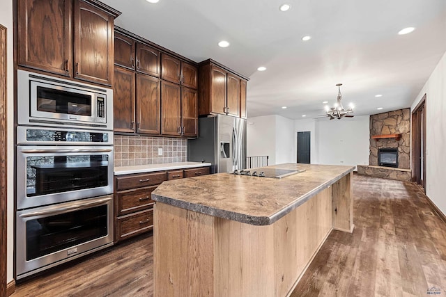 kitchen with appliances with stainless steel finishes, tasteful backsplash, a fireplace, a center island, and a chandelier