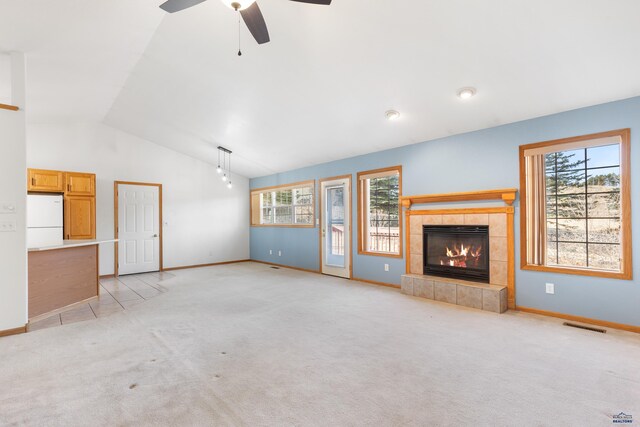 unfurnished living room featuring light carpet, vaulted ceiling, ceiling fan, plenty of natural light, and a tiled fireplace