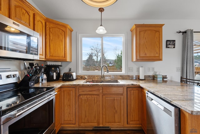 kitchen with pendant lighting, light stone counters, sink, and appliances with stainless steel finishes