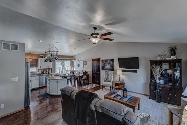 living room featuring ceiling fan with notable chandelier, a textured ceiling, dark hardwood / wood-style flooring, and lofted ceiling