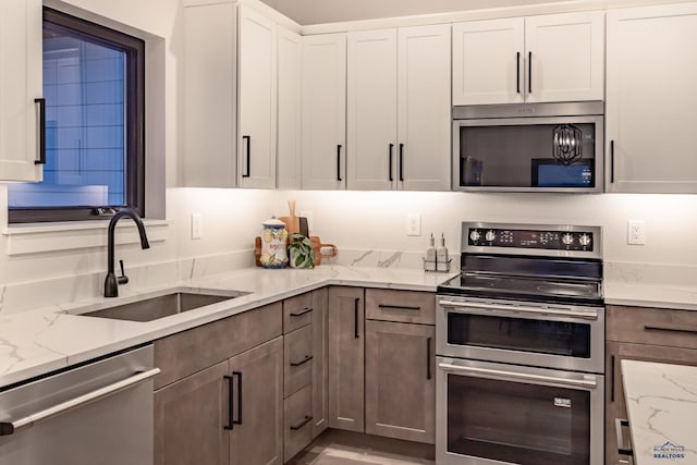 kitchen featuring light stone countertops, appliances with stainless steel finishes, white cabinetry, and sink