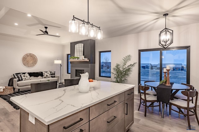 kitchen featuring pendant lighting, ceiling fan with notable chandelier, light stone countertops, a fireplace, and a kitchen island