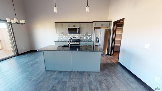 kitchen with hanging light fixtures, tasteful backsplash, dark stone countertops, a center island with sink, and appliances with stainless steel finishes