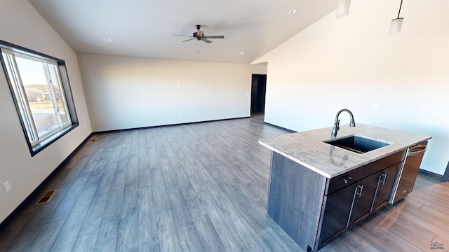 kitchen with sink, dishwasher, light stone counters, lofted ceiling, and a kitchen island with sink