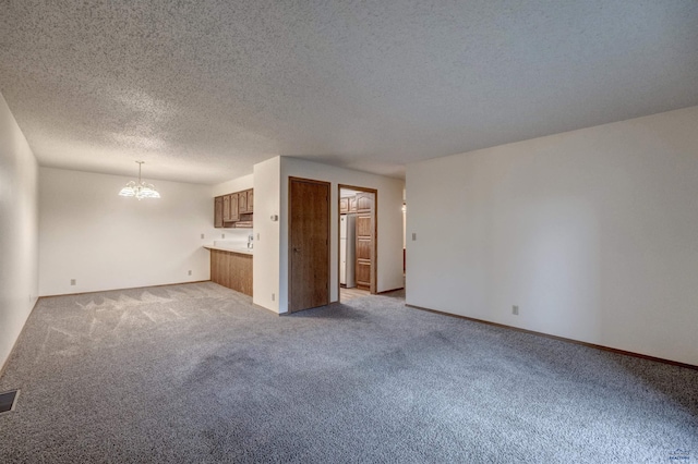 unfurnished living room with light carpet, a textured ceiling, and a notable chandelier