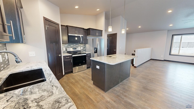 kitchen featuring light stone countertops, appliances with stainless steel finishes, sink, a center island, and hanging light fixtures