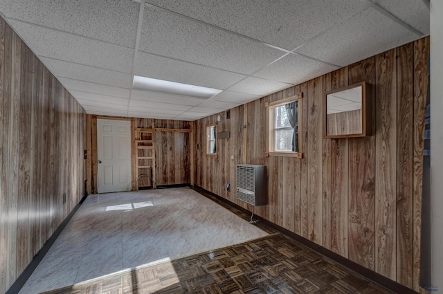 empty room featuring dark parquet floors, heating unit, a drop ceiling, and wood walls