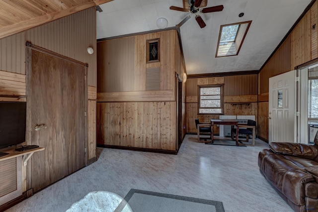 living room with vaulted ceiling with skylight, ceiling fan, wood walls, and wood ceiling