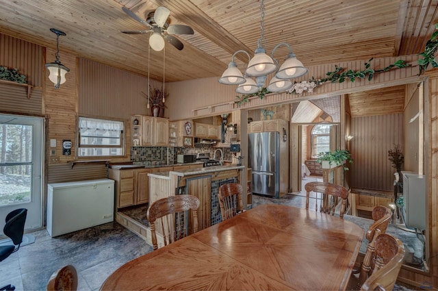 dining room with ceiling fan with notable chandelier, wood ceiling, and wooden walls