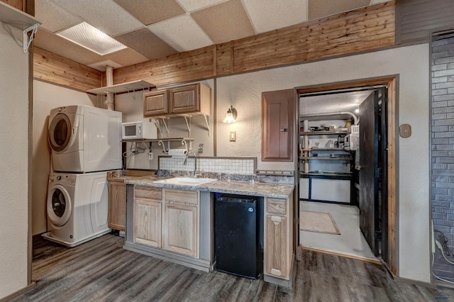 kitchen with light brown cabinets, stacked washer and dryer, sink, decorative backsplash, and black dishwasher